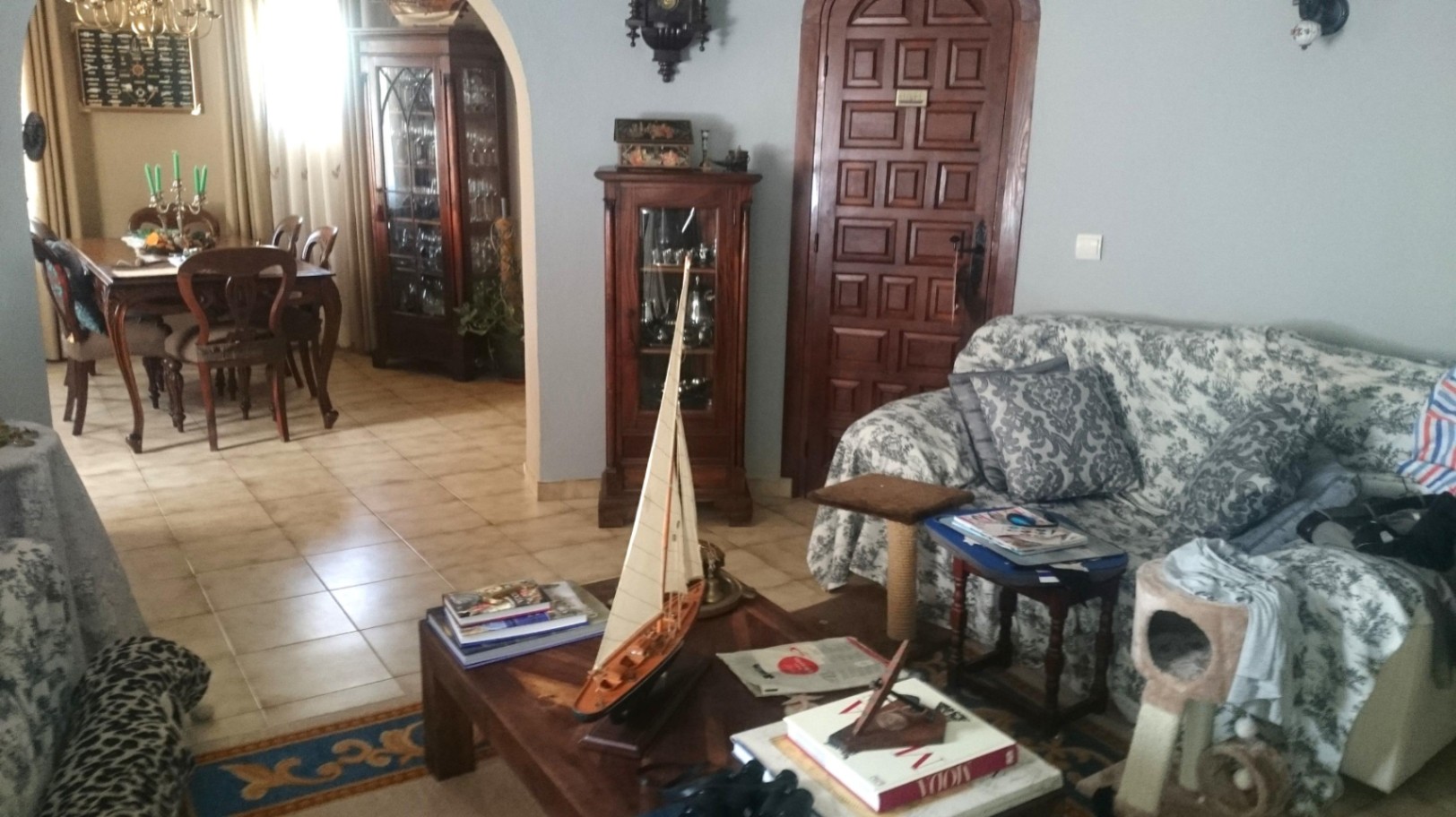 Salón comedor de estilo tradicional con suelos cerámicos, muebles de madera oscura, vitrinas clásicas y un arco que conecta ambas estancias.