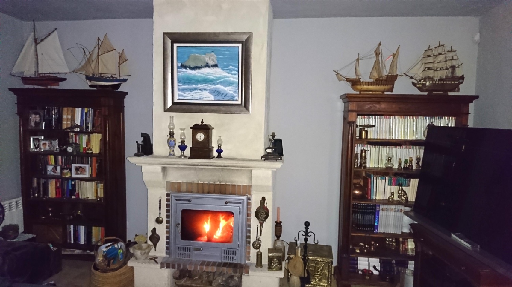 Salón con chimenea de piedra y casete de leña, flanqueada por estanterías de madera clásica con maquetas navales y decoración tradicional.