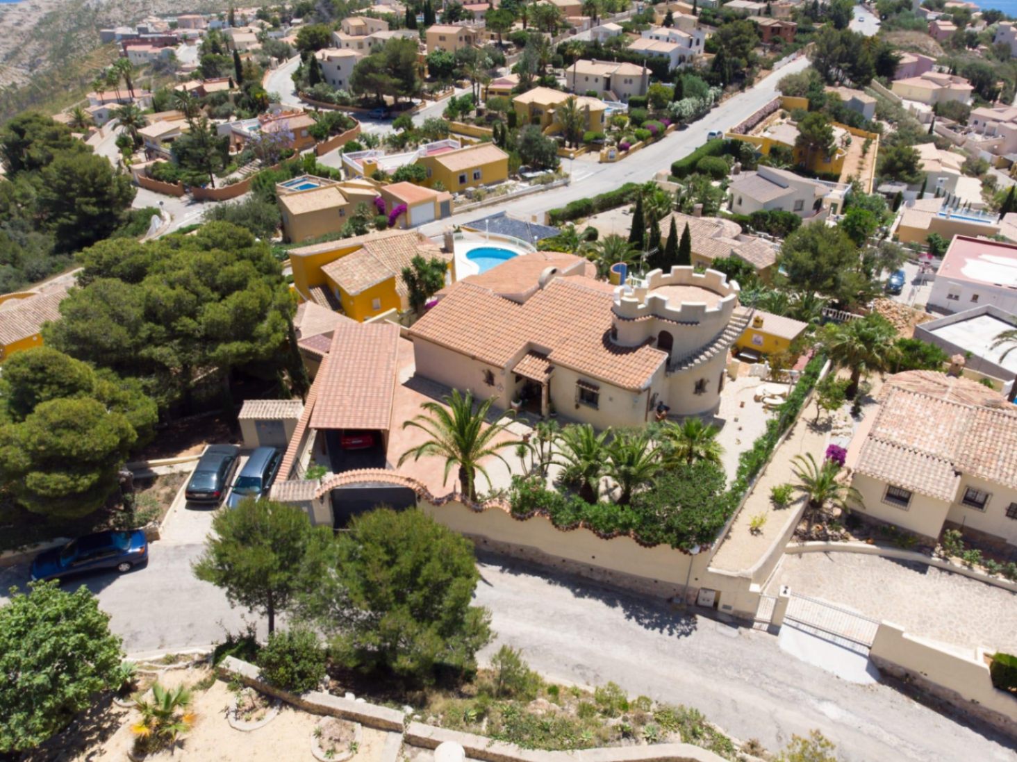 Vista aérea de la villa de estilo mediterráneo destacando su torreón circular almenado, tejado de teja cerámica y jardín con palmeras maduras en Cumbre del Sol.