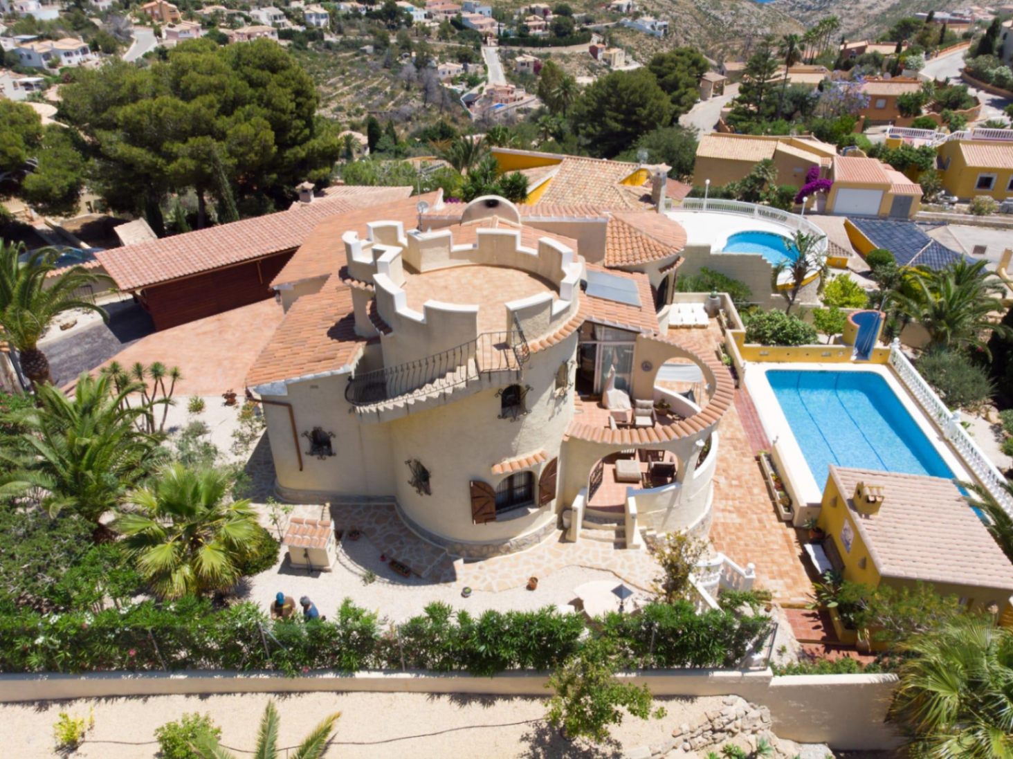 Vista aérea de la villa destacando su torre circular con terraza almenada, la piscina rectangular y la zona de cocina exterior rodeada de vegetación mediterránea.