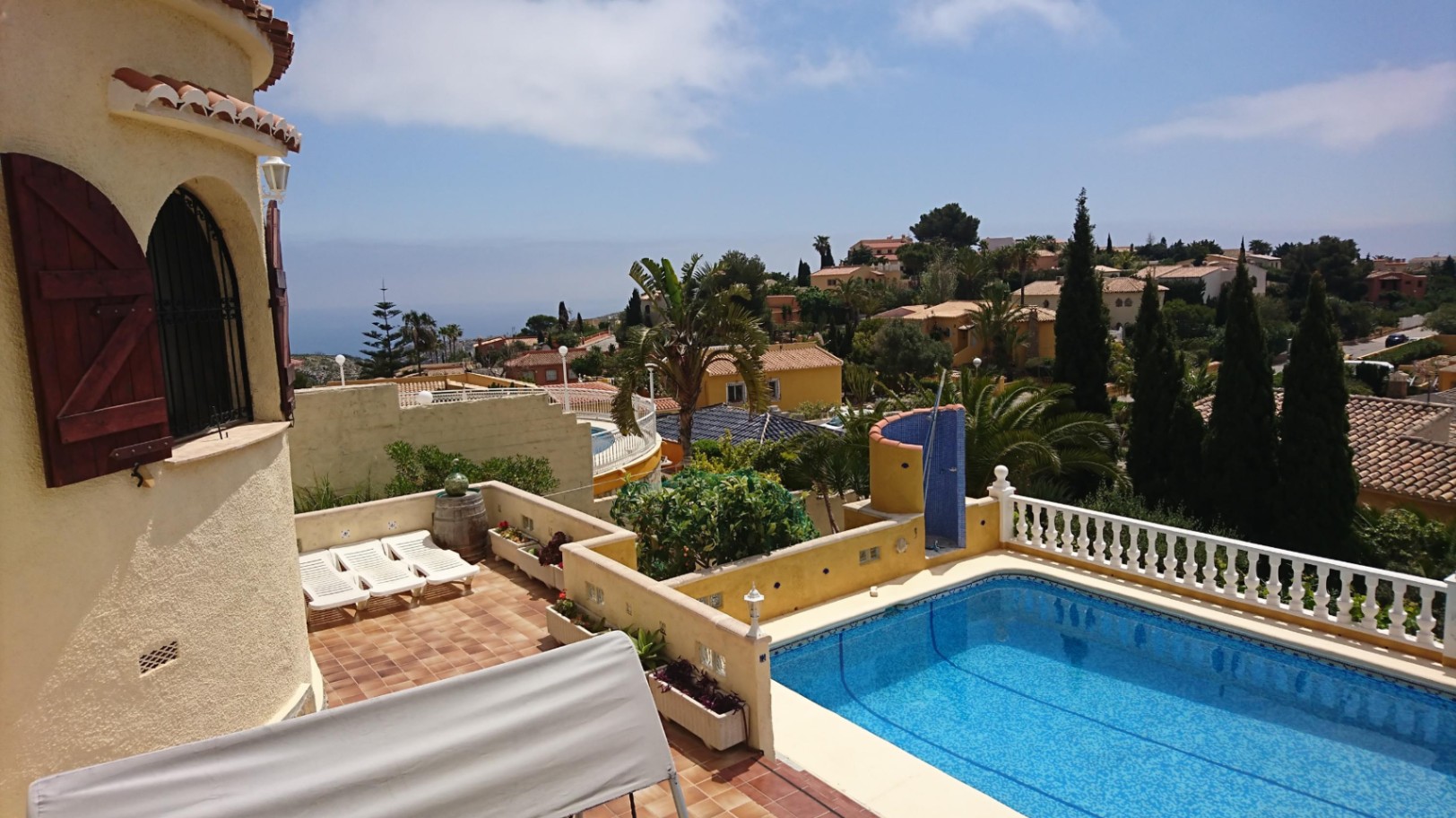 Vista exterior de la piscina rectangular con terraza de terracota, balaustrada blanca y torre con contraventanas de madera, orientada hacia el mar Mediterráneo.