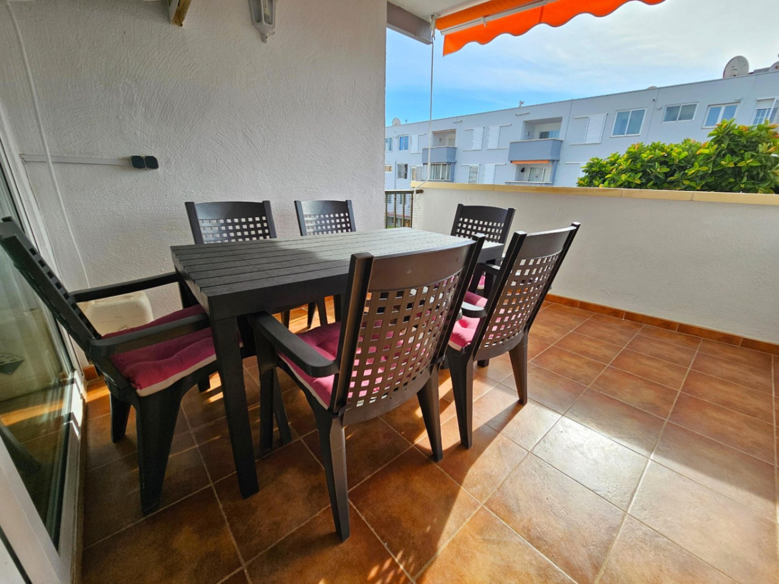 Amplia terraza con suelo cerámico de tonos terracota, equipada con un conjunto de comedor exterior y un toldo retráctil naranja para mayor confort.