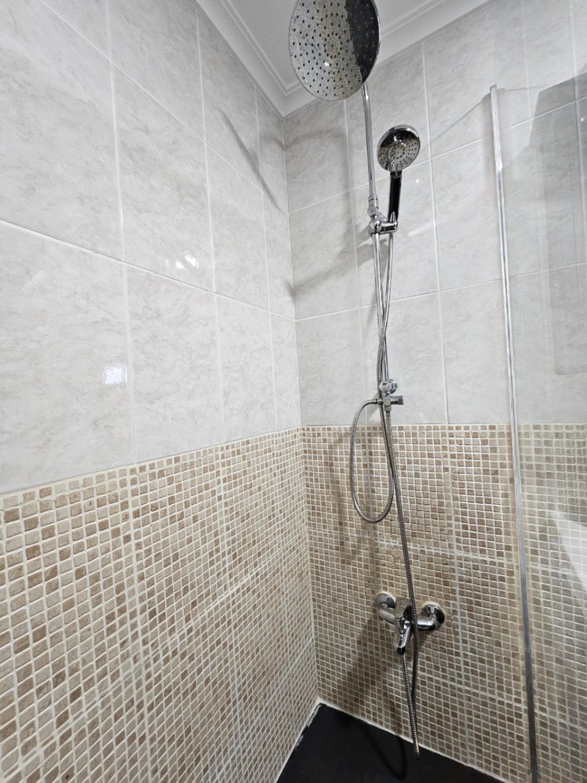 Ducha contemporánea con sistema de doble rociador, revestimiento de gresite en tonos tierra y azulejos de gran formato con efecto mármol.