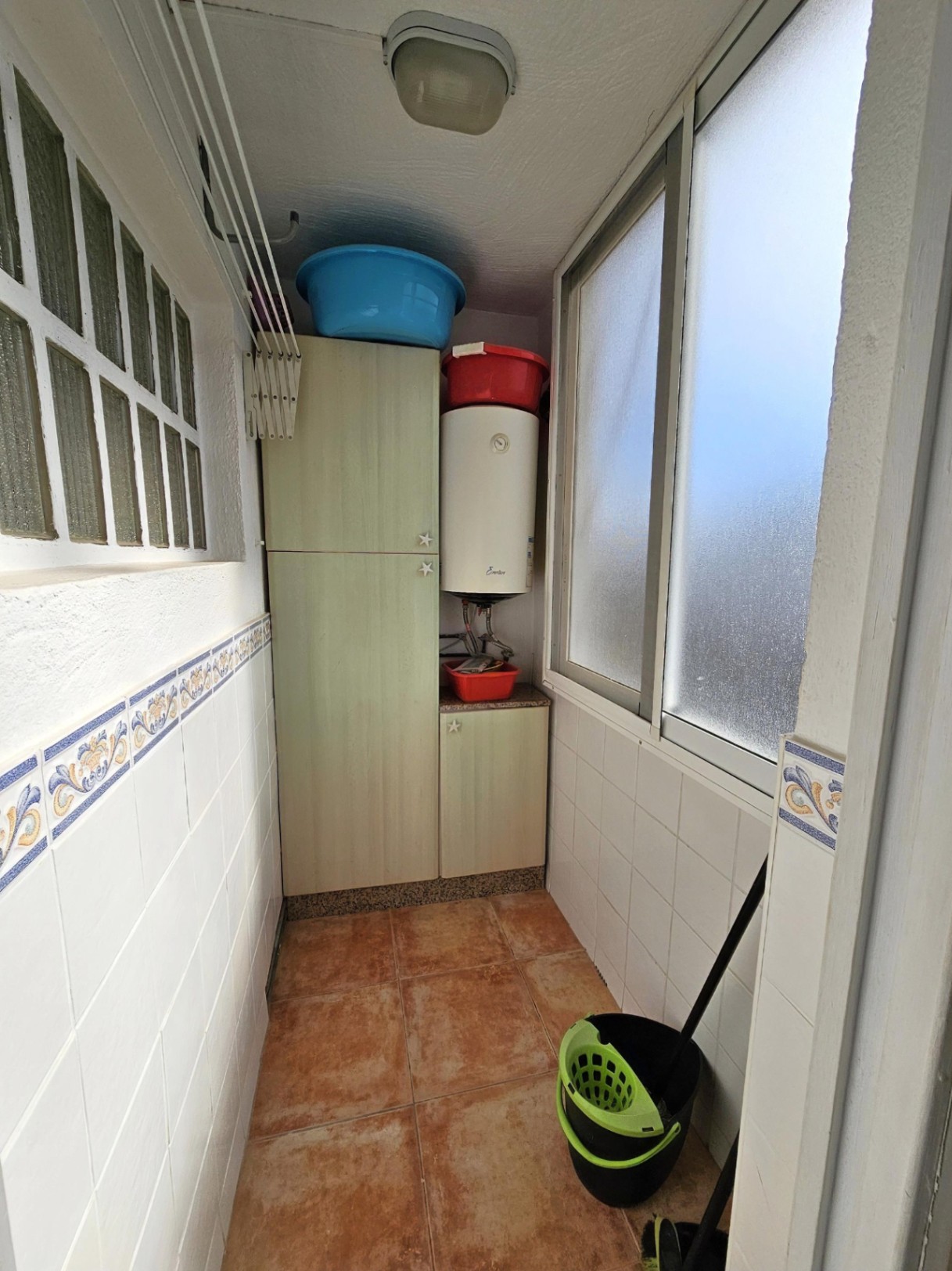 Lavadero funcional con armarios de almacenaje, calentador eléctrico, tendedero de pared y suelos de gres rústico.