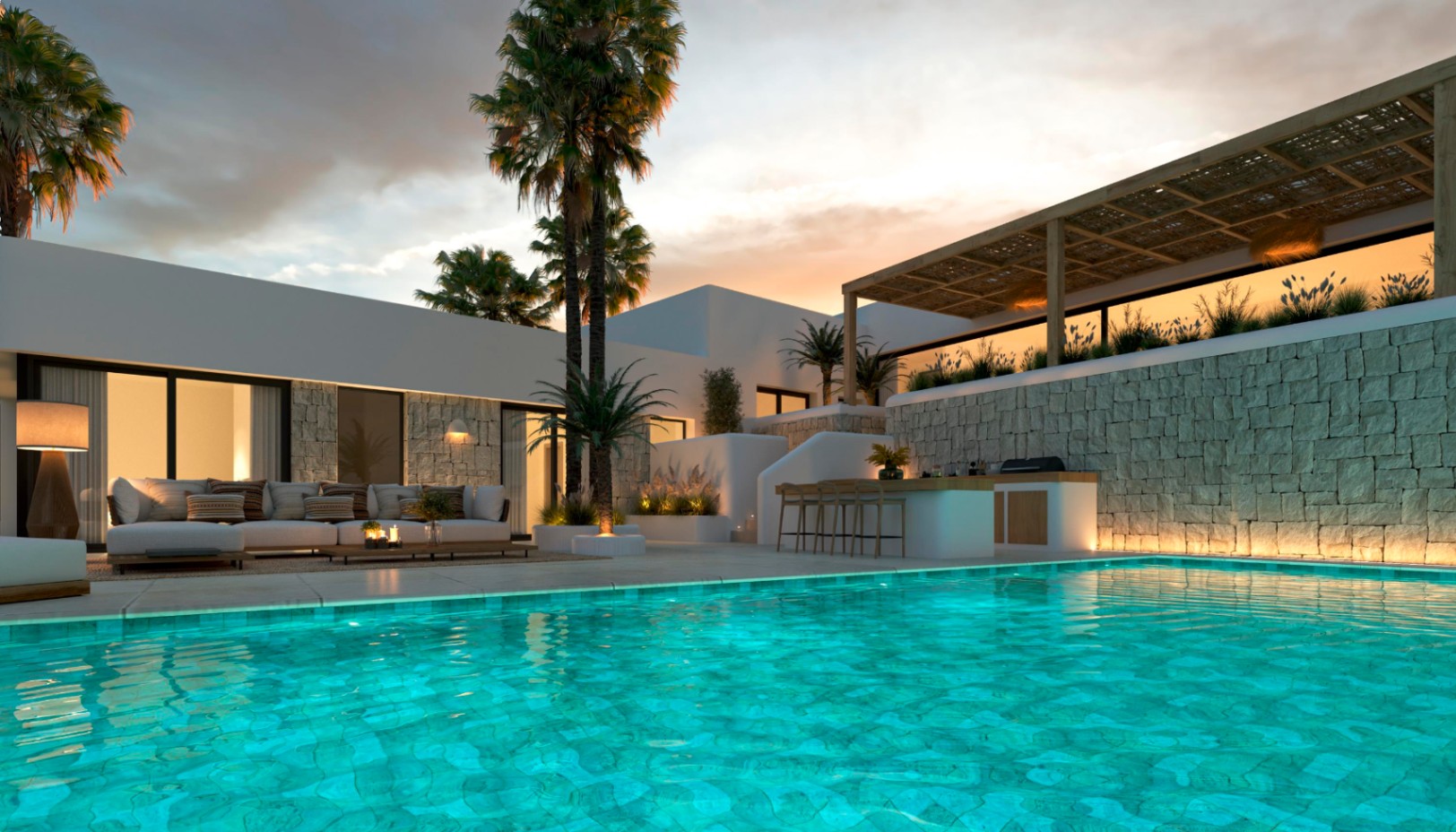 Zona exterior con piscina iluminada, cocina de verano y salón lounge. Destacan los muros de piedra natural, la pérgola de madera y el paisajismo con palmeras bajo el atardecer.