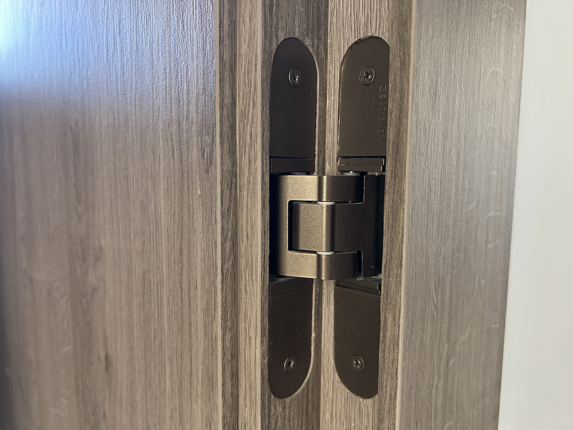 Detalle de bisagra oculta de alta gama en acabado bronce, integrada en carpintería de madera oscura para un diseño minimalista y funcional.