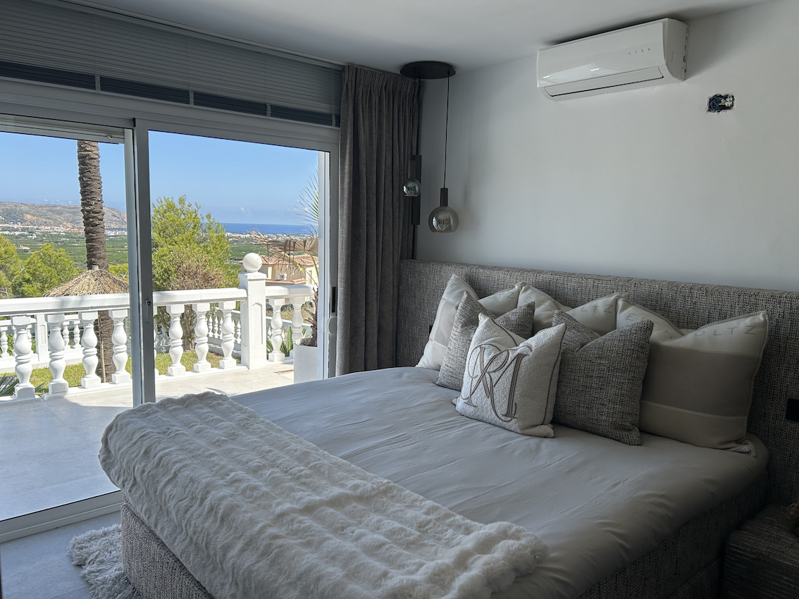 Dormitorio principal con acceso directo a terraza privada, vistas panorámicas al mar y aire acondicionado. Presenta textiles en tonos grises y blancos.