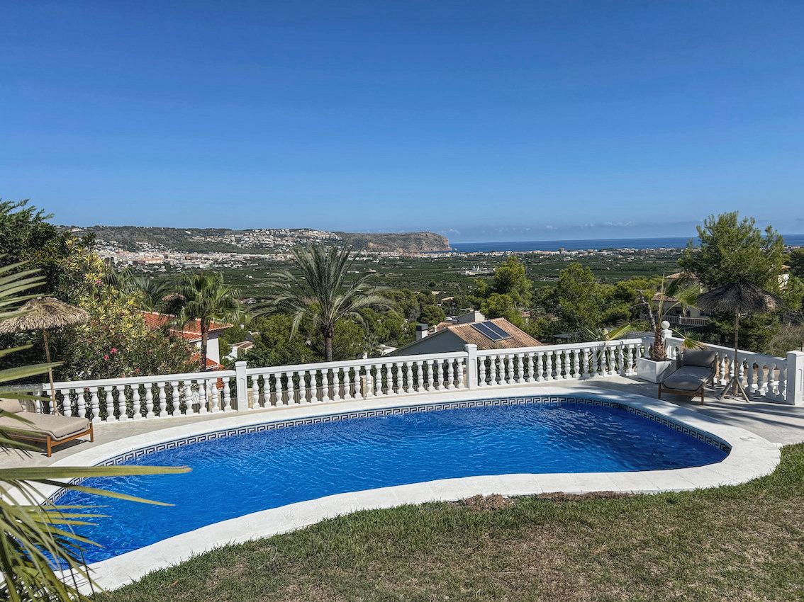 Piscina exterior de forma curva con balaustrada blanca, ofreciendo vistas panorámicas al valle y al mar Mediterráneo bajo un cielo despejado.