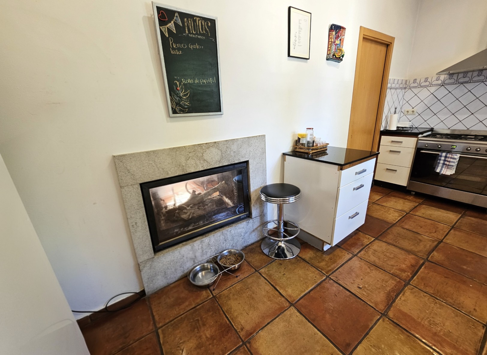 Cocina con suelos de barro artesanales, chimenea integrada con marco de piedra y mobiliario funcional junto a una zona de cocción con acabados en acero inoxidable.