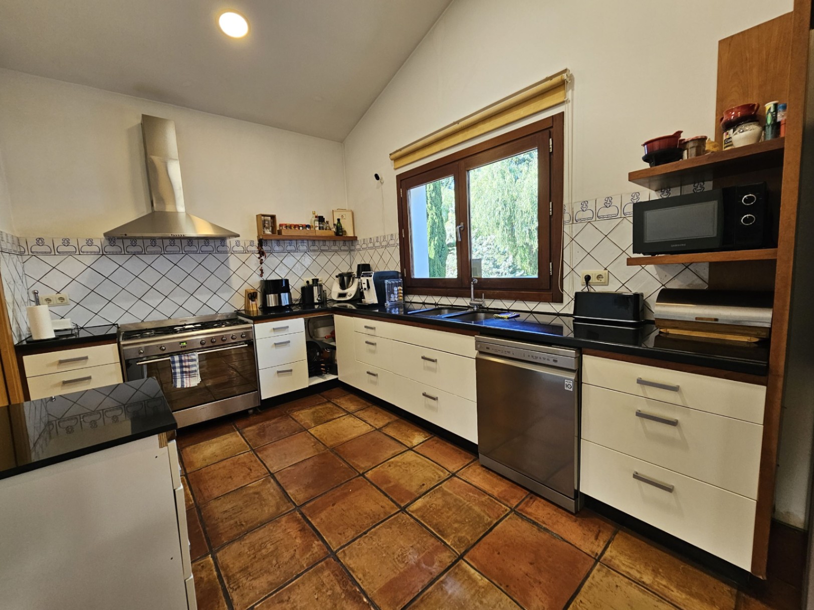 Cocina equipada con suelos de barro artesanal, encimeras de piedra negra y azulejos decorativos pintados a mano. Dispone de electrodomésticos de acero inoxidable y techos inclinados.