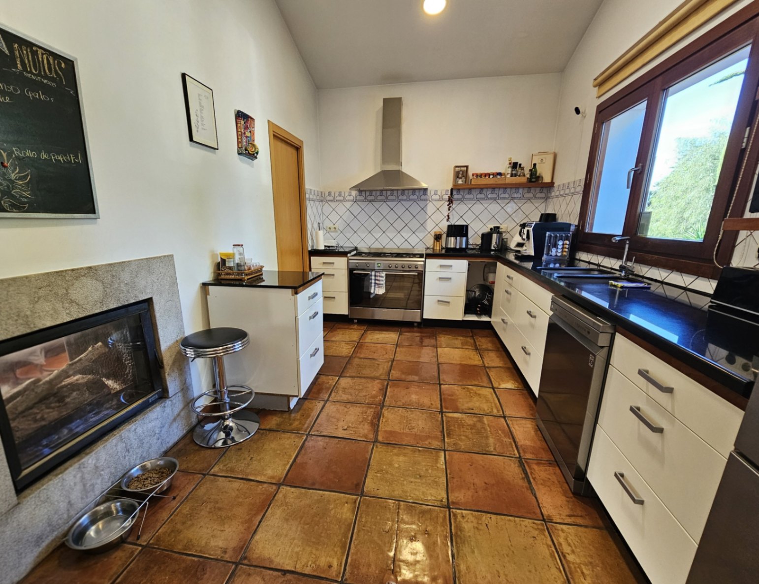Cocina equipada con suelos de barro hechos a mano, encimeras oscuras y una chimenea de doble cara integrada en una estructura de piedra.