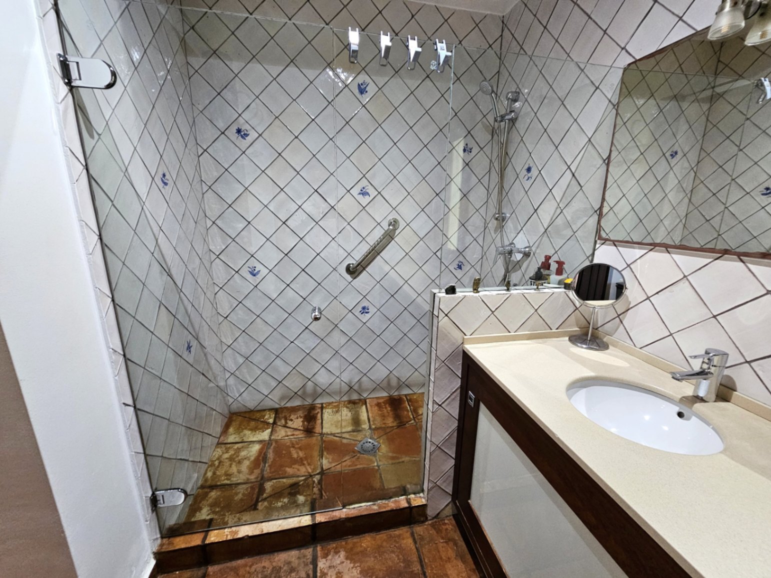 Cuarto de baño con azulejos pintados a mano en disposición diagonal, ducha de obra con mampara de cristal y suelos de barro cocido artesanales.