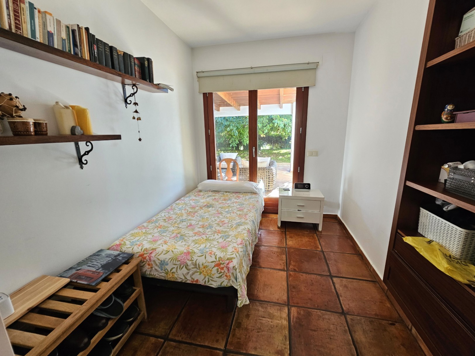 Dormitorio individual con suelos de barro manual, estanterías de madera y acceso directo a la naya exterior a través de grandes ventanales.