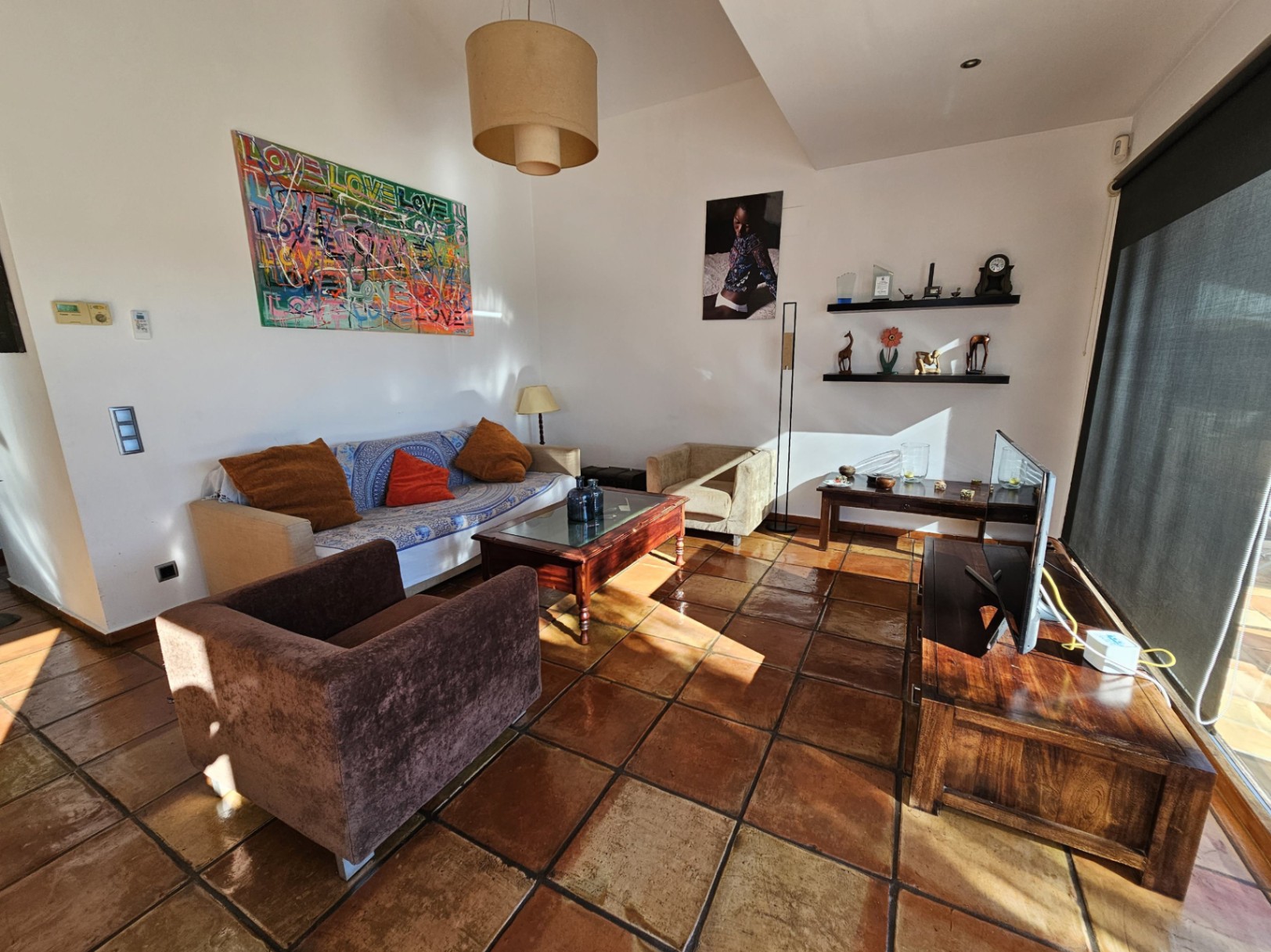 Salón con suelos de barro hechos a mano, mobiliario de madera y gran luminosidad natural. Destaca la decoración artística y el acceso a través de amplios ventanales.