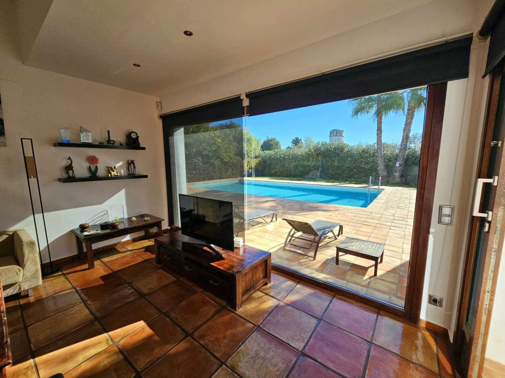 Salón con suelos de barro hechos a mano y grandes ventanales de seguridad que conectan el interior con la terraza de terracota y la piscina.