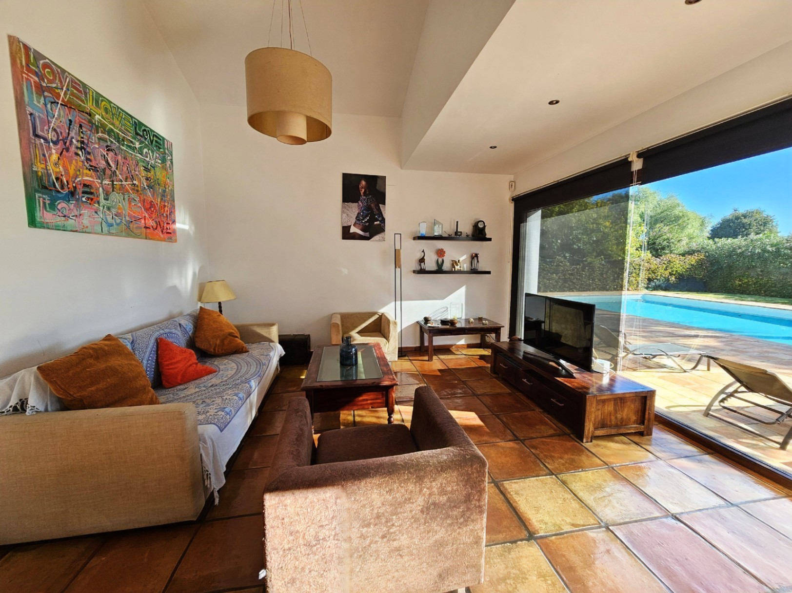 Salón con suelos de barro hechos a mano y grandes ventanales de seguridad que conectan el interior con la zona de piscina y el jardín.
