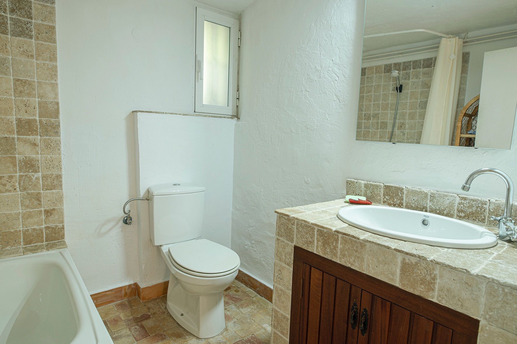 Cuarto de baño de estilo rústico con encimera de piedra natural, mueble de madera oscura, sanitarios blancos y bañera integrada.