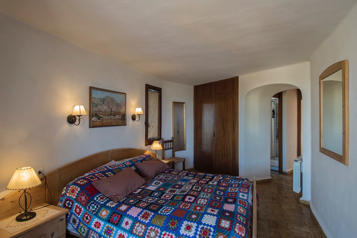 Dormitorio de estilo rústico con armarios empotrados de madera, suelos cerámicos y un arco arquitectónico que conecta con el baño privado.