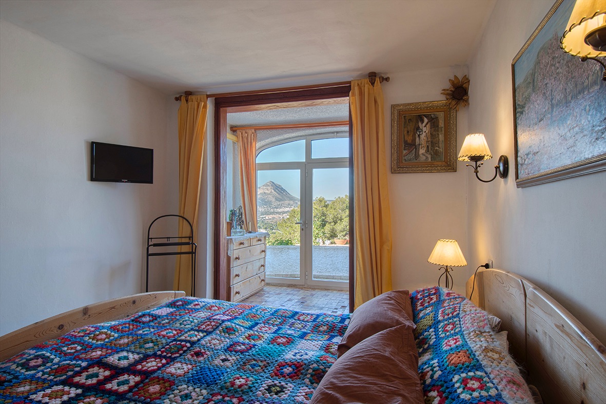 Dormitorio de estilo rústico con mobiliario de madera, colcha artesanal y acceso directo a una terraza con vistas despejadas a la montaña.