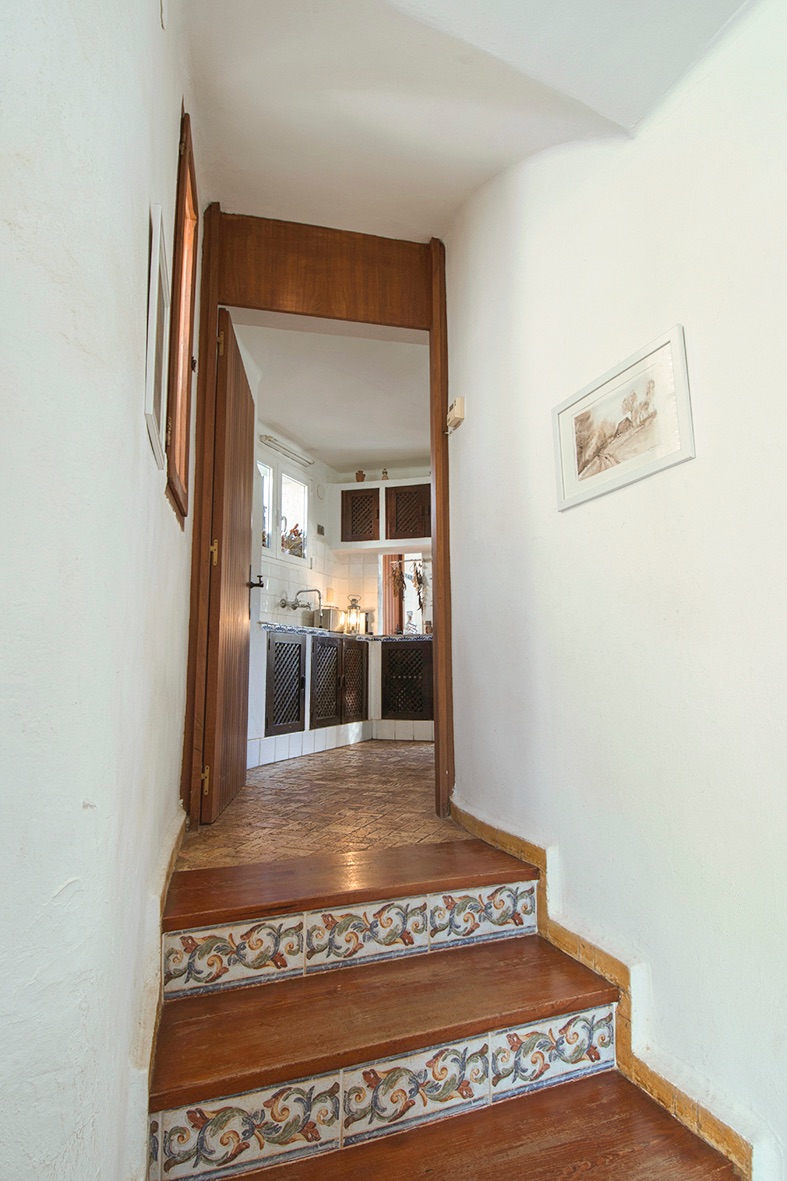 Escalera con peldaños de madera y azulejos decorativos que da paso a una cocina de estilo rústico con armarios de madera oscura y celosía.