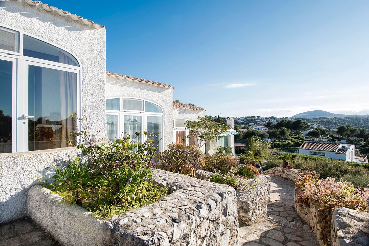 Fachada de estilo tradicional con muros de piedra natural, ventanales en arco y vistas panorámicas al valle y las montañas bajo un cielo despejado.