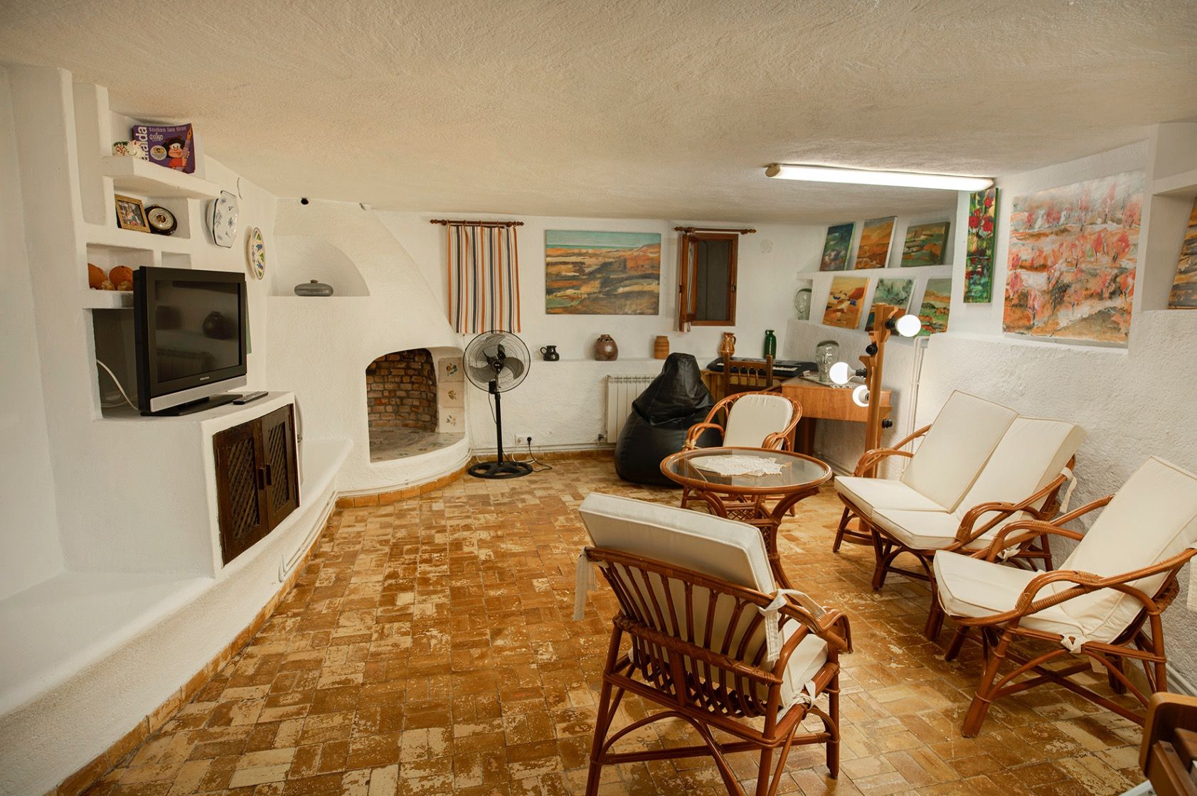 Salón de estilo rústico con paredes de yeso blanco, chimenea de obra redondeada, suelo de terracota y mobiliario de bambú con cojines claros.