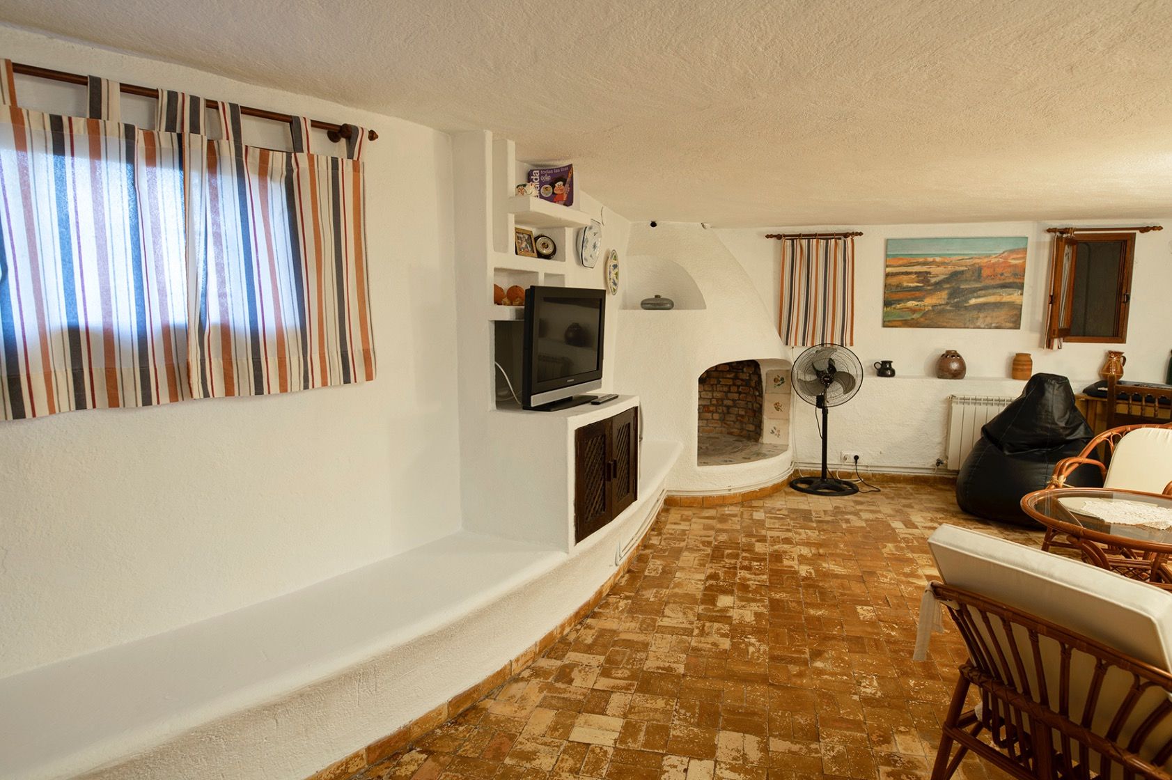 Salón rústico en planta baja con chimenea de leña integrada, suelos de terracota y paredes blancas con estanterías de obra tradicionales.