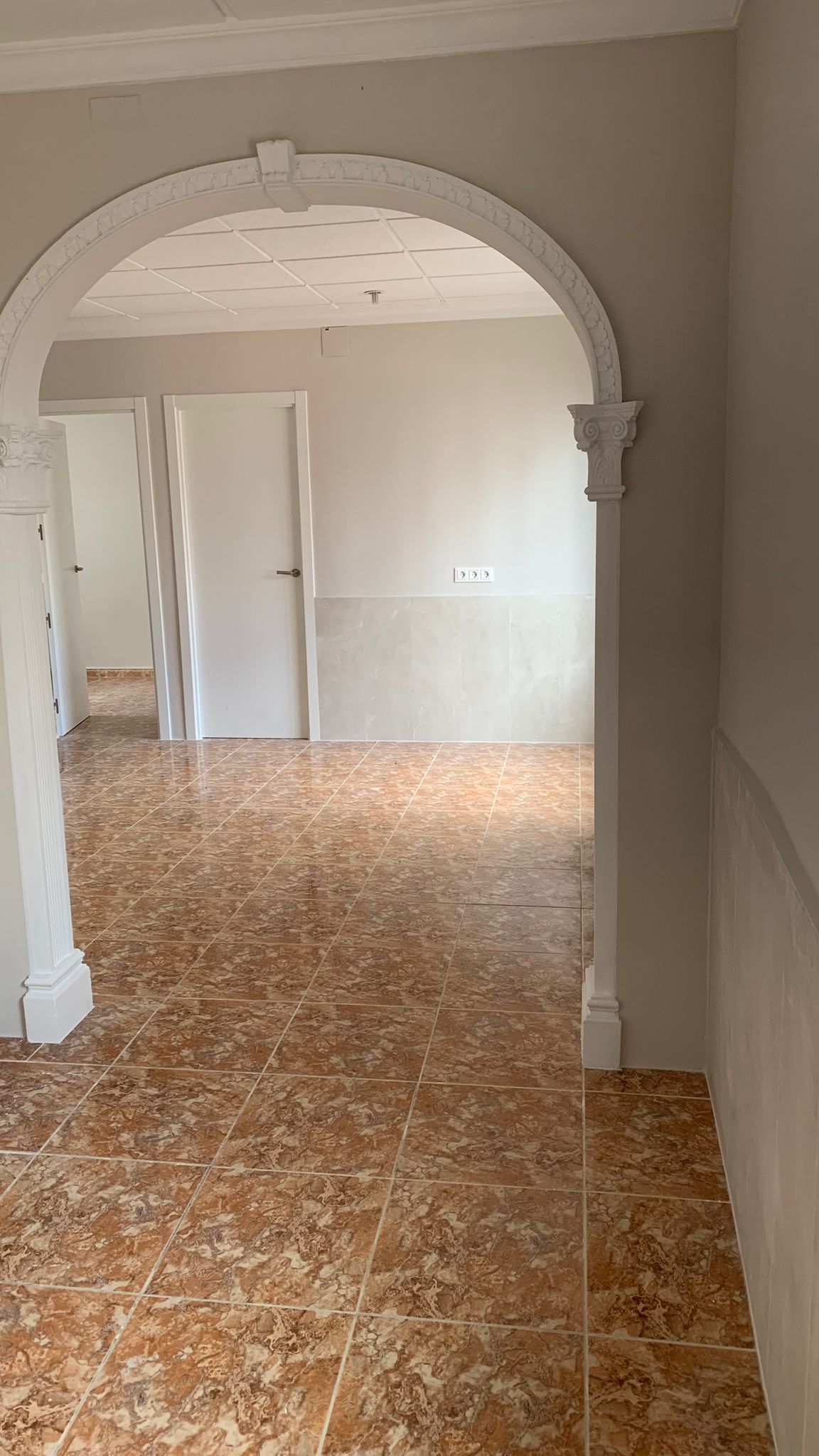 Distribuidor con arco decorativo de estilo clásico, suelos de gres veteado en tonos tierra y puertas interiores blancas que dan acceso a las estancias.