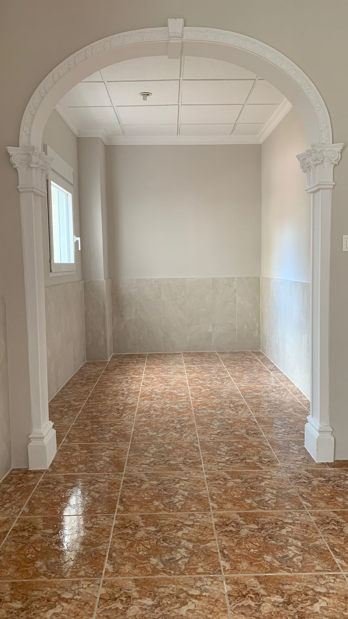 Entrada con arco decorativo clásico, suelos de gres cerámico en tonos tierra y paredes con zócalo de azulejo claro.