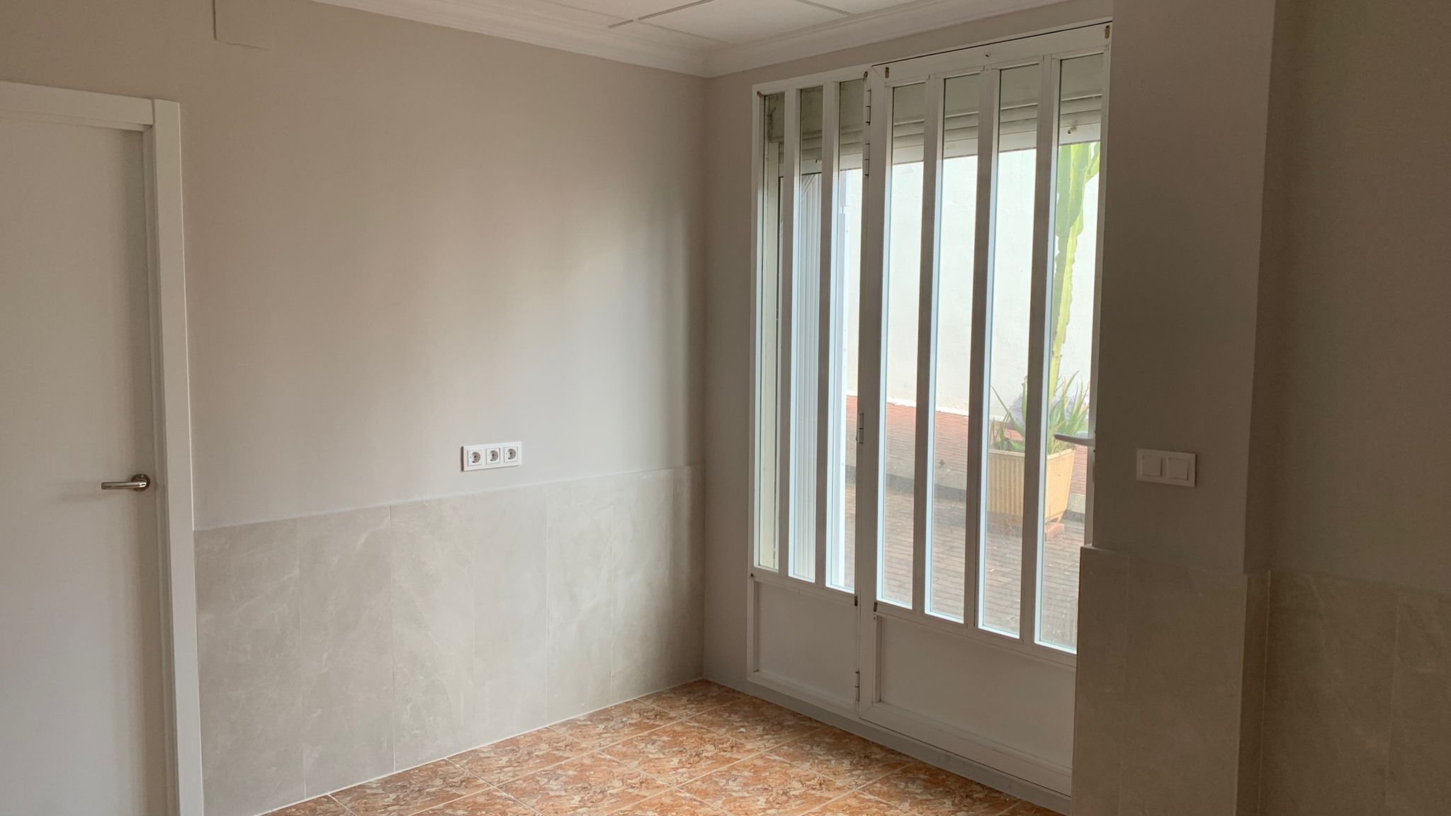 Habitación con suelos de gres y zócalo efecto mármol, equipada con una puerta acristalada con rejas de seguridad que comunica con el patio exterior.