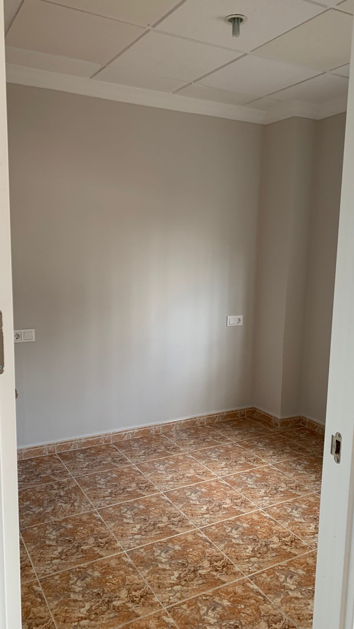 Habitación interior reformada con suelos de gres efecto mármol marrón, paredes en tono neutro y techo técnico de placas desmontables.