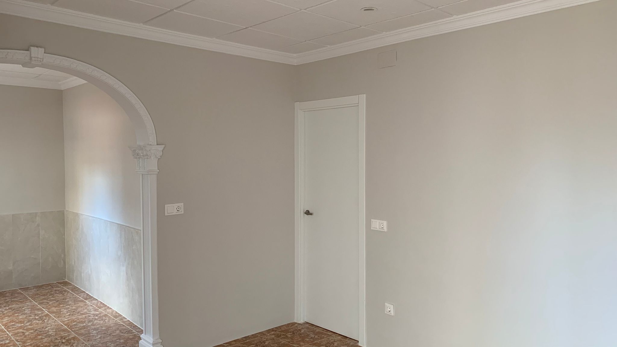 Interior reformado con paredes en tonos neutros, suelos de gres y un arco decorativo con molduras clásicas que conecta las estancias.
