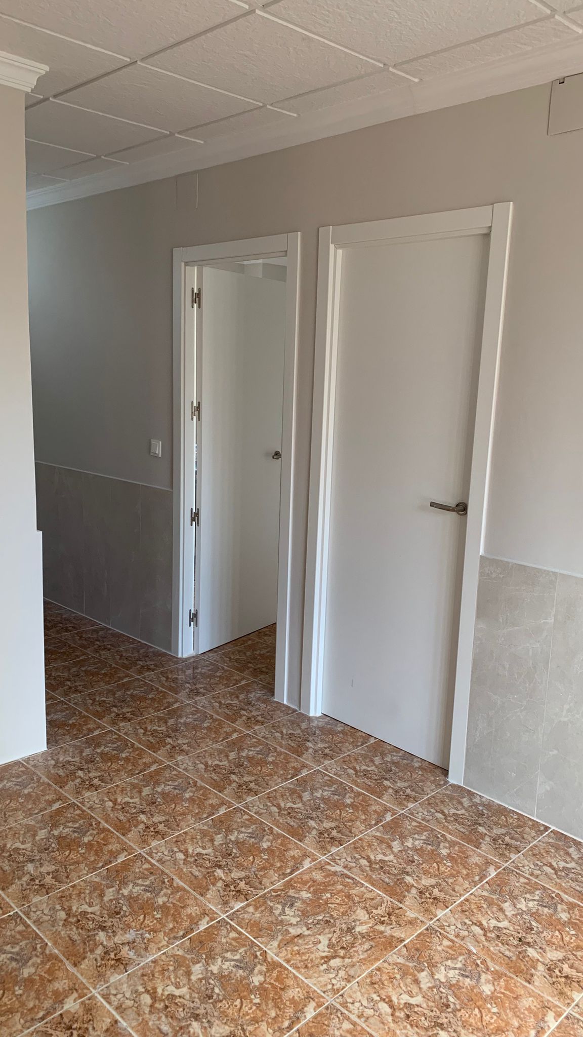 Pasillo con suelos cerámicos marmoleados, carpintería interior en blanco y paredes con zócalo de gres porcelánico en tonos neutros.