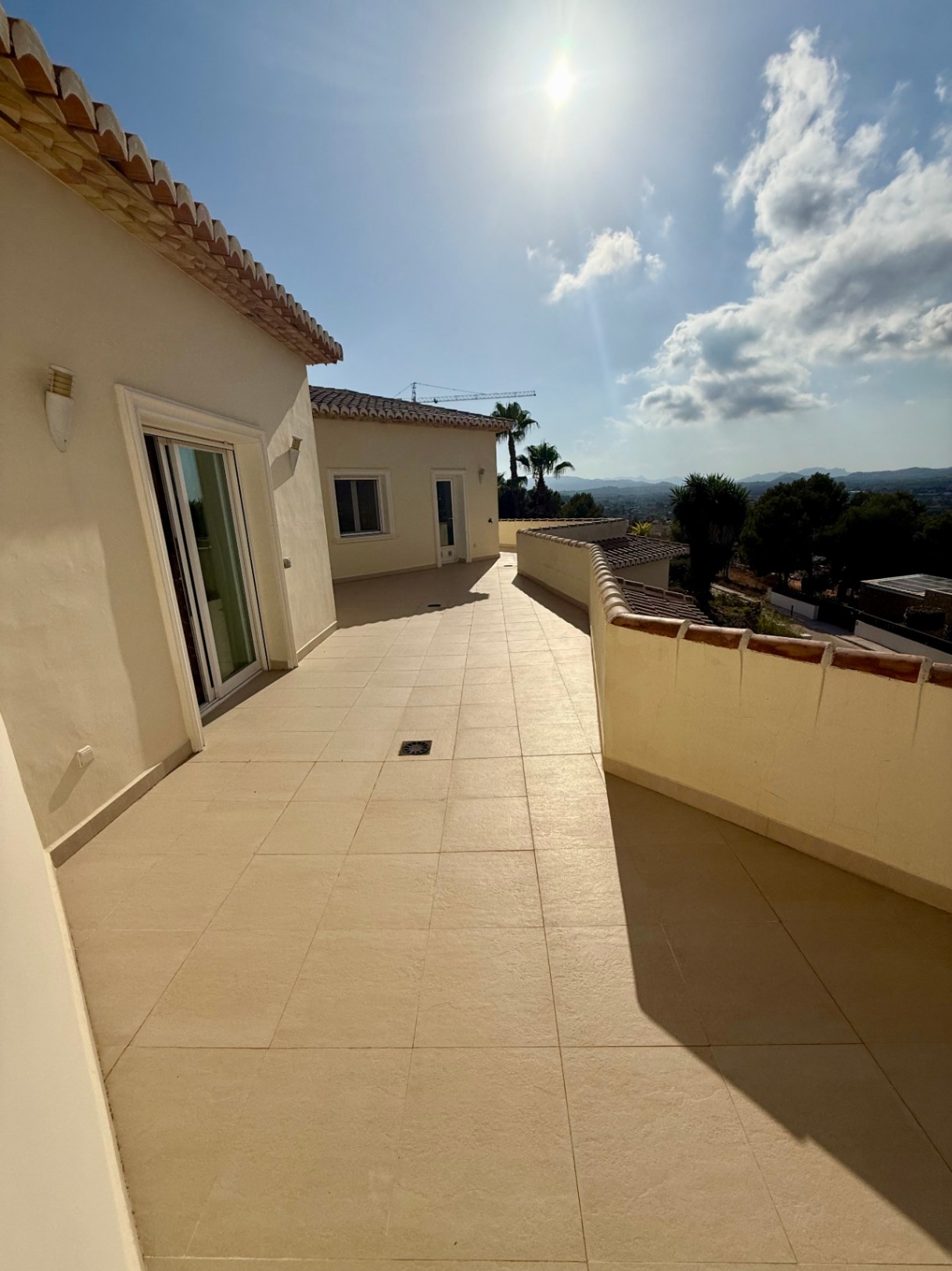 Amplia terraza en la planta superior con suelos cerámicos de tono arena y vistas despejadas al valle de Jávea bajo el sol mediterráneo.
