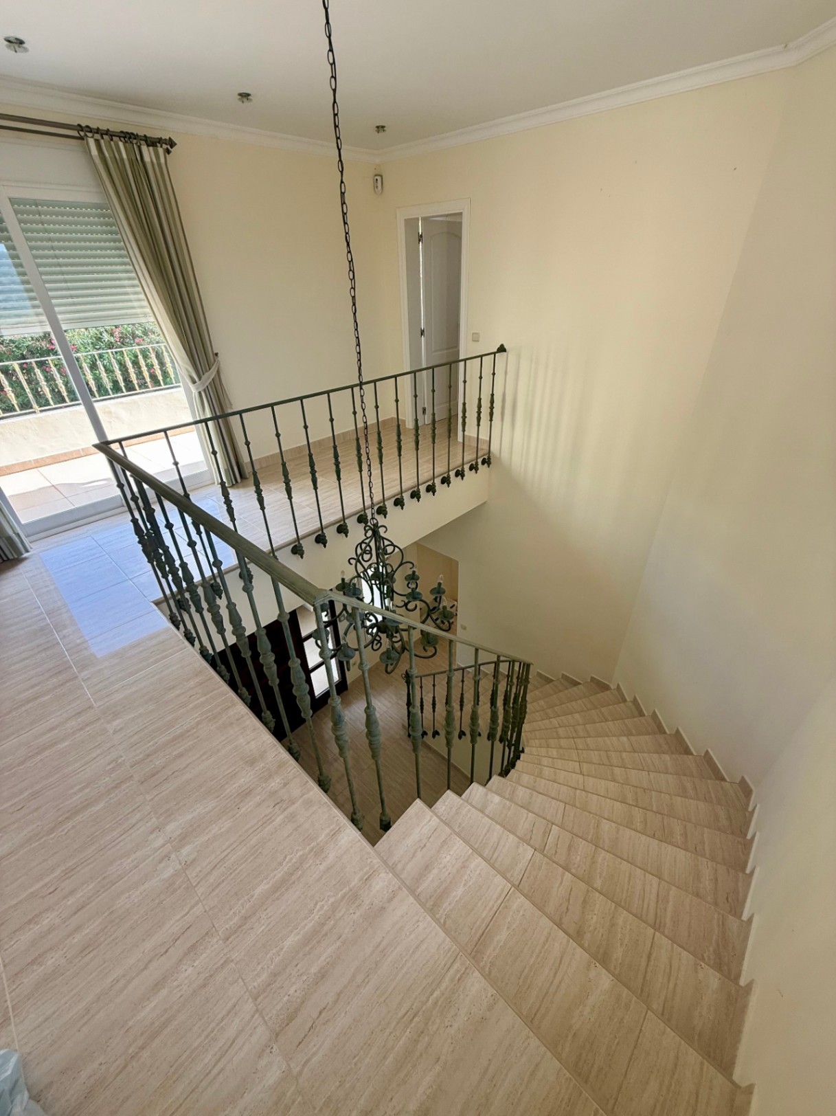 Escalera curva de piedra natural con barandilla de hierro forjado, que comunica con un rellano luminoso y acceso directo a la terraza superior.