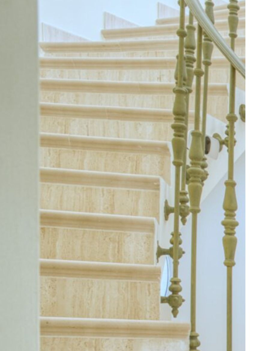 Escalera de piedra natural con peldaños de mármol pulido y una barandilla metálica de diseño clásico y ornamental que conecta los niveles de la villa.