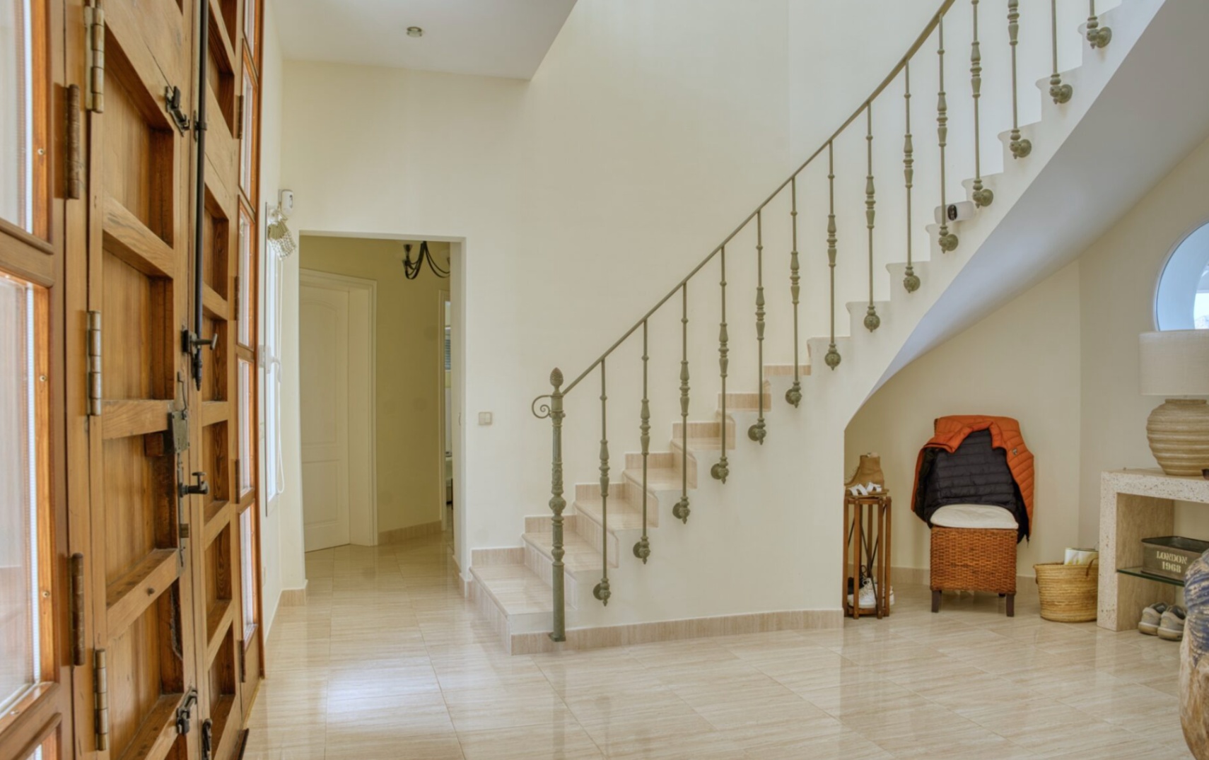 Hall de entrada con puerta de madera maciza, suelos de mármol pulido y una escalera curva con barandilla de hierro forjado ornamental.