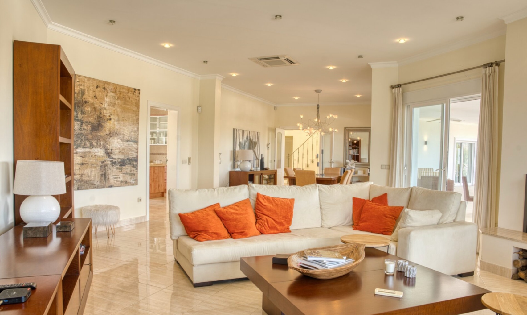Salón espacioso con suelos de mármol pulido, sofá en L blanco con detalles en naranja y acceso directo a la terraza mediante grandes ventanales correderos.