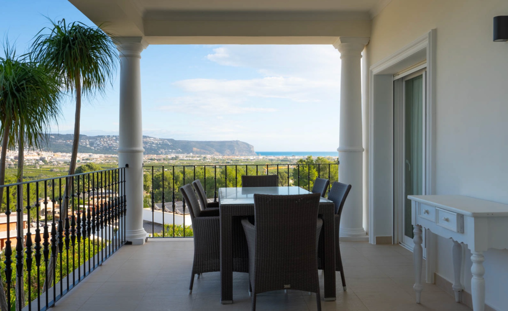 Terraza cubierta con columnas clásicas y barandilla de forja, ofreciendo un comedor exterior con vistas panorámicas al valle de Jávea y al mar Mediterráneo.