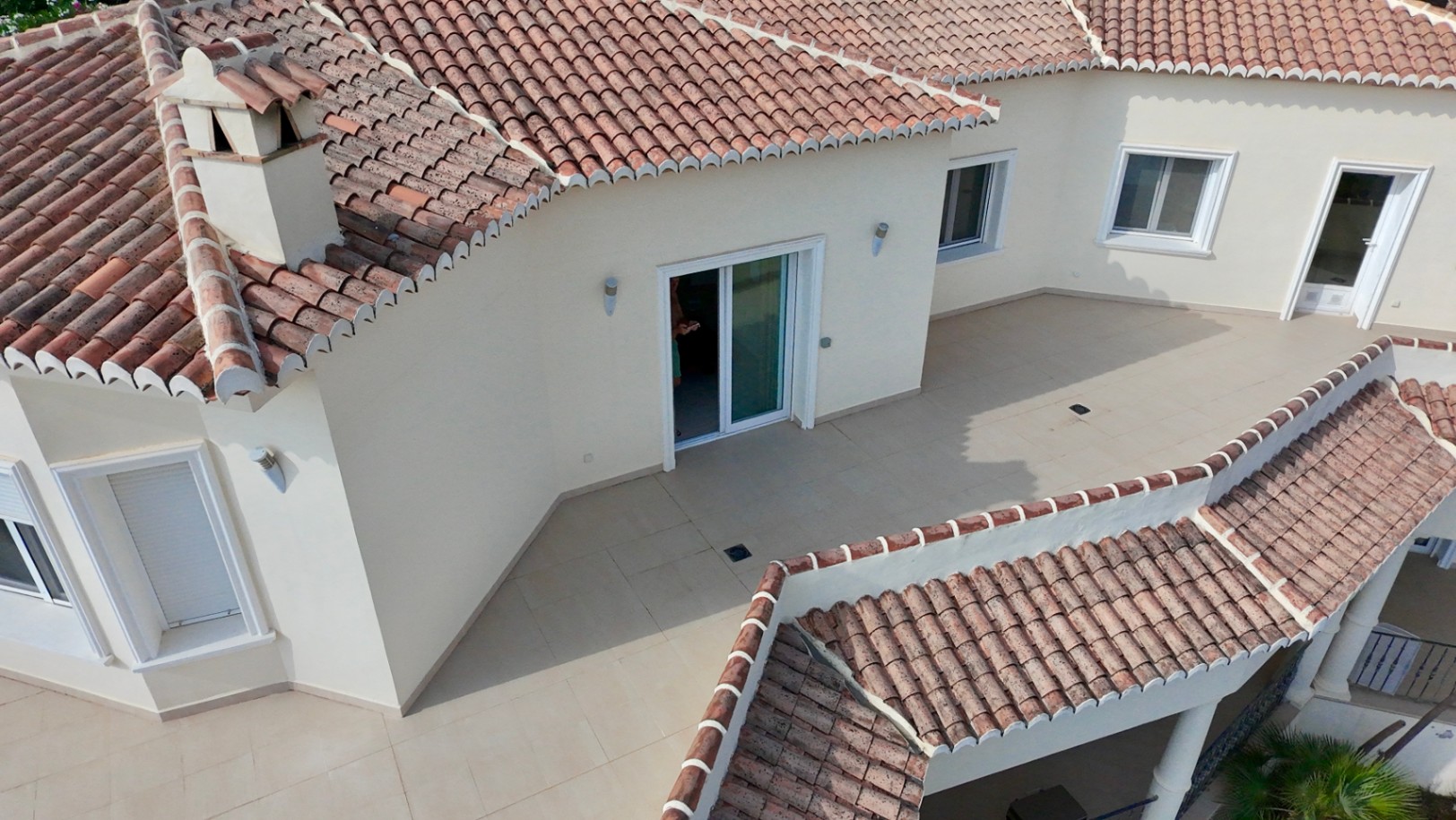 Vista aérea de la terraza superior con suelos cerámicos y acceso directo, destacando la arquitectura mediterránea con tejados de teja tradicional y acabados en tonos crema.